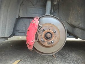 Close-up of a car's exposed brake disc and red brake caliper during maintenance.