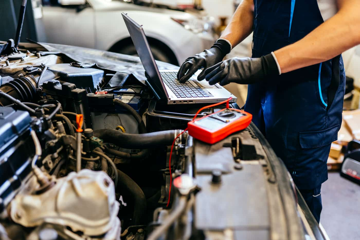 Mechanic using a laptop and diagnostic tools to analyse a car engine in a professional workshop.