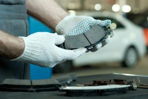 Mechanic wearing gloves inspecting new brake pads in an automotive workshop.