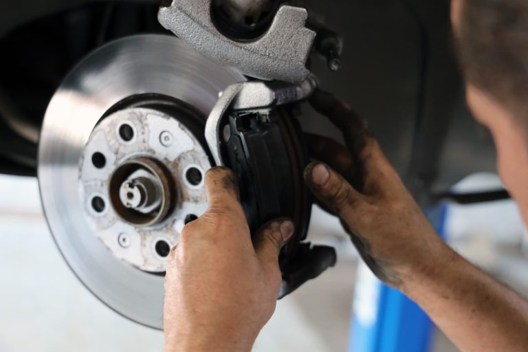 Mechanic inspecting and replacing a car brake pad in a workshop.