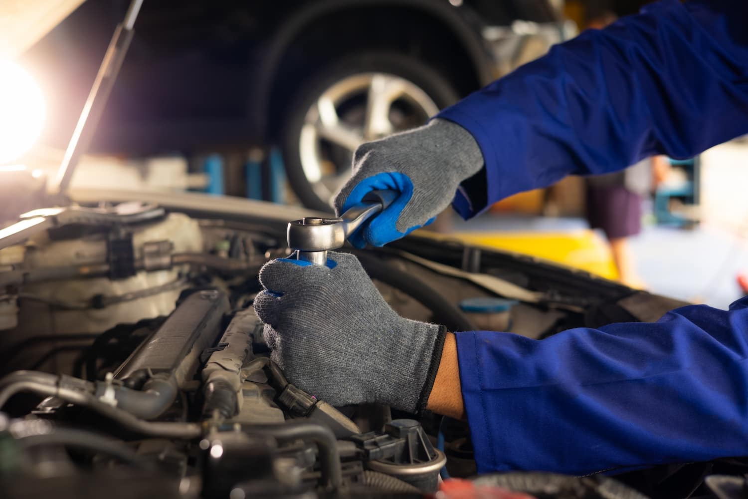 Mechanic wearing blue gloves and uniform using a ratchet tool to repair a car engine in a professional workshop.