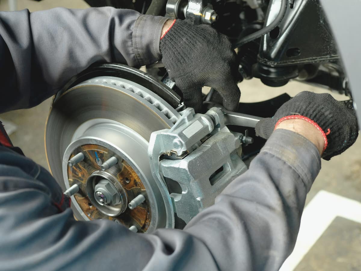 Mechanic repairing a car's brake system, focusing on the brake disc and caliper in a workshop.