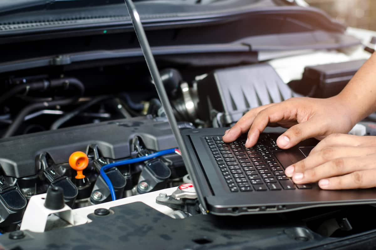 Mechanic using a laptop for engine diagnostics and tuning under the hood of a car.